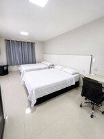Quarto de hotel com três camas, uma escrivaninha e uma cadeira.