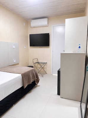 Une chambre d’hôtel équipée d’un lit, d’un téléviseur à écran plat, d’un distributeur d’eau, d’une chaise et d’un réfrigérateur.