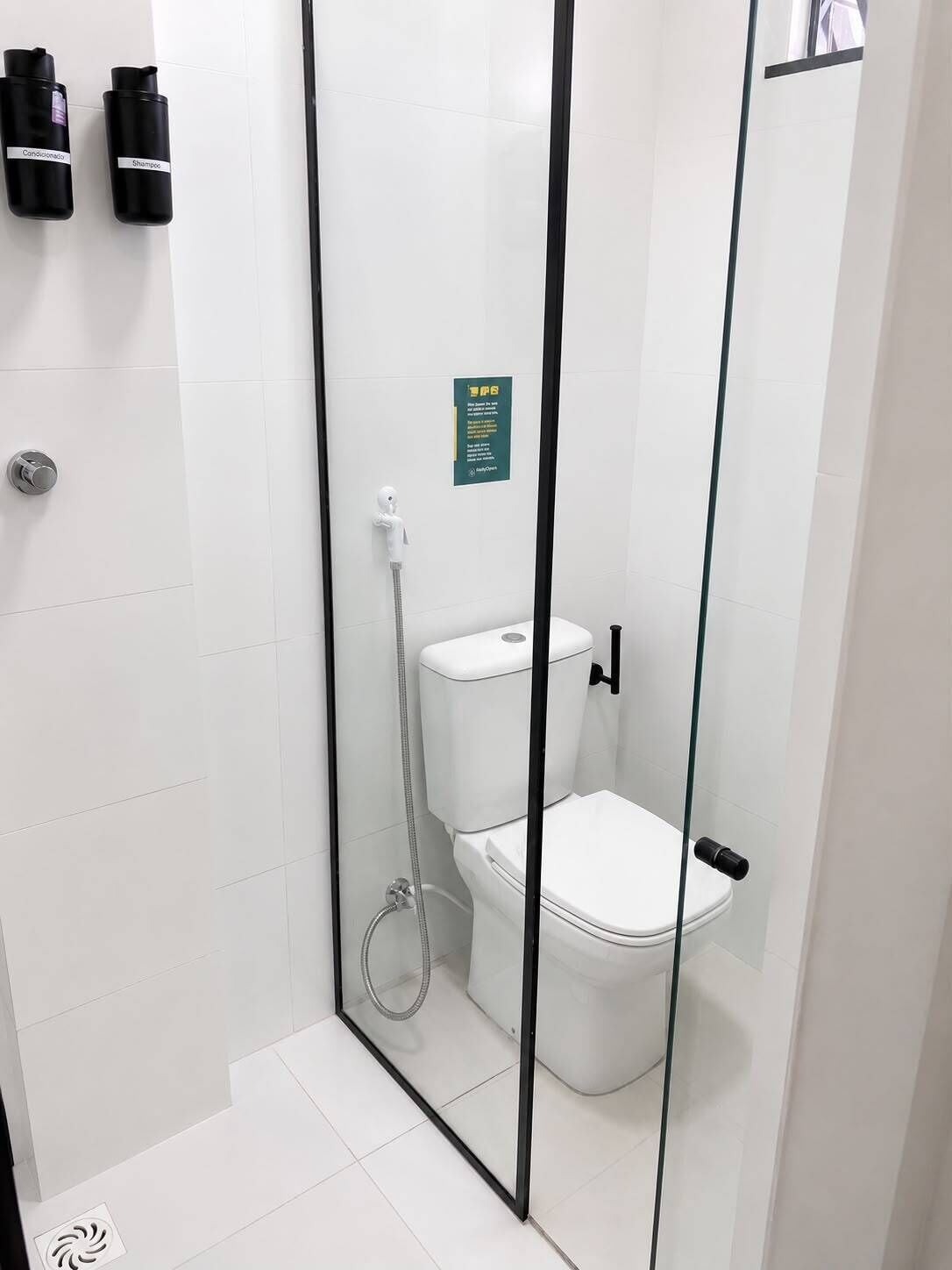 A modern bathroom with a glass shower enclosure, a toilet, and two black shampoo bottles on the wall.