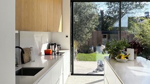 A modern kitchen with white cabinets, a wooden upper section, and a large sliding glass door leading to a garden. - Large, architect designed family home with garden close to tube in North London (London)