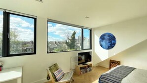 A modern bedroom with large windows, a bed, a desk, and a bookshelf. - Large, architect designed family home with garden close to tube in North London (London)