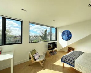 A modern bedroom with large windows, a bed, a desk, and a bookshelf. - Large, architect designed family home with garden close to tube in North London (London)