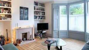 A living room with a fireplace, bookshelves, a television, and a glass coffee table. - Large, architect designed family home with garden close to tube in North London (London)