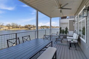 Une terrasse couverte avec vue sur un lac, comprenant une table, des chaises et un ventilateur de plafond.