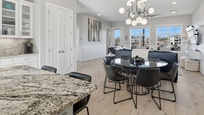 A modern kitchen with granite countertops, a dining area with a round table and chairs, and a view of a residential neighborhood. - GiGi's Jewel | Lakefront+ Pool+ Pet Friendly +Lift (Kingsland)