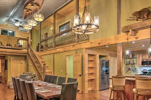 Ein geräumiger Essbereich mit einem langen Holztisch und mehreren Stühlen, eine Treppe, die zu einer oberen Ebene führt, und ein Küchenbereich mit modernen Geräten.