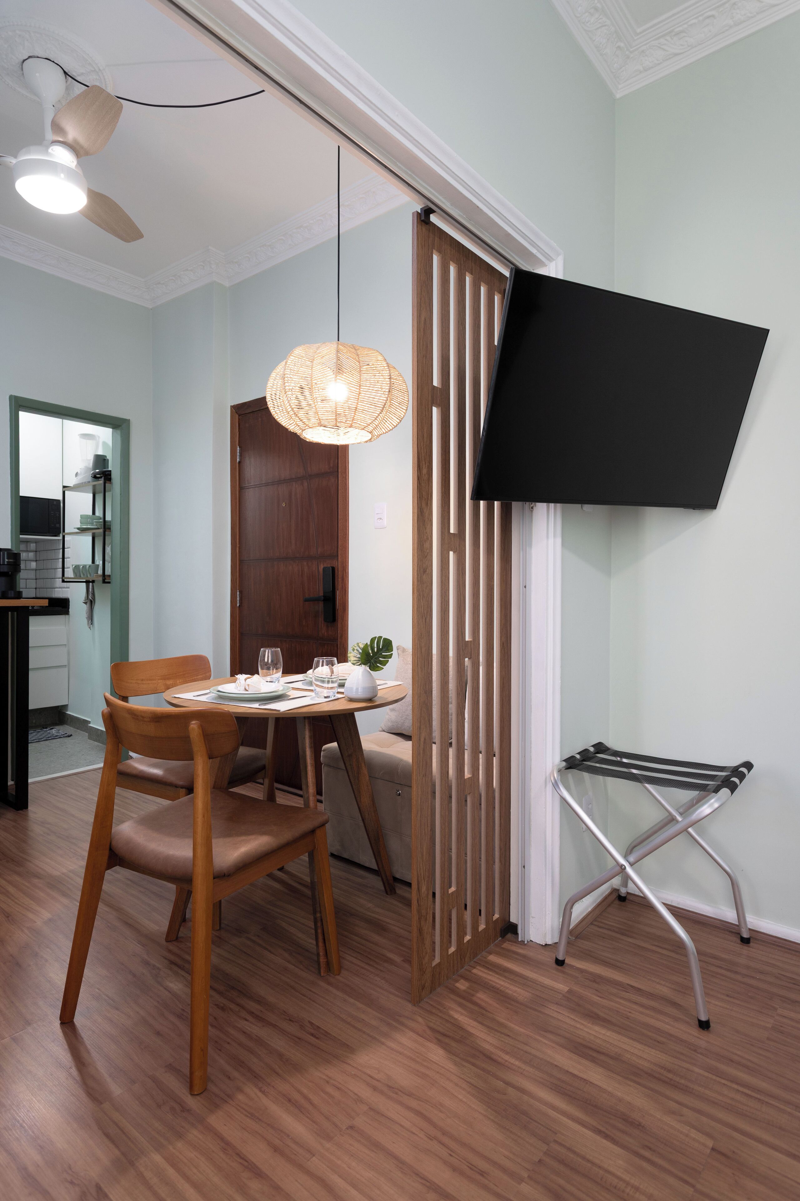 A dining area with a wooden table, chairs, a ceiling fan, and a wall-mounted TV.