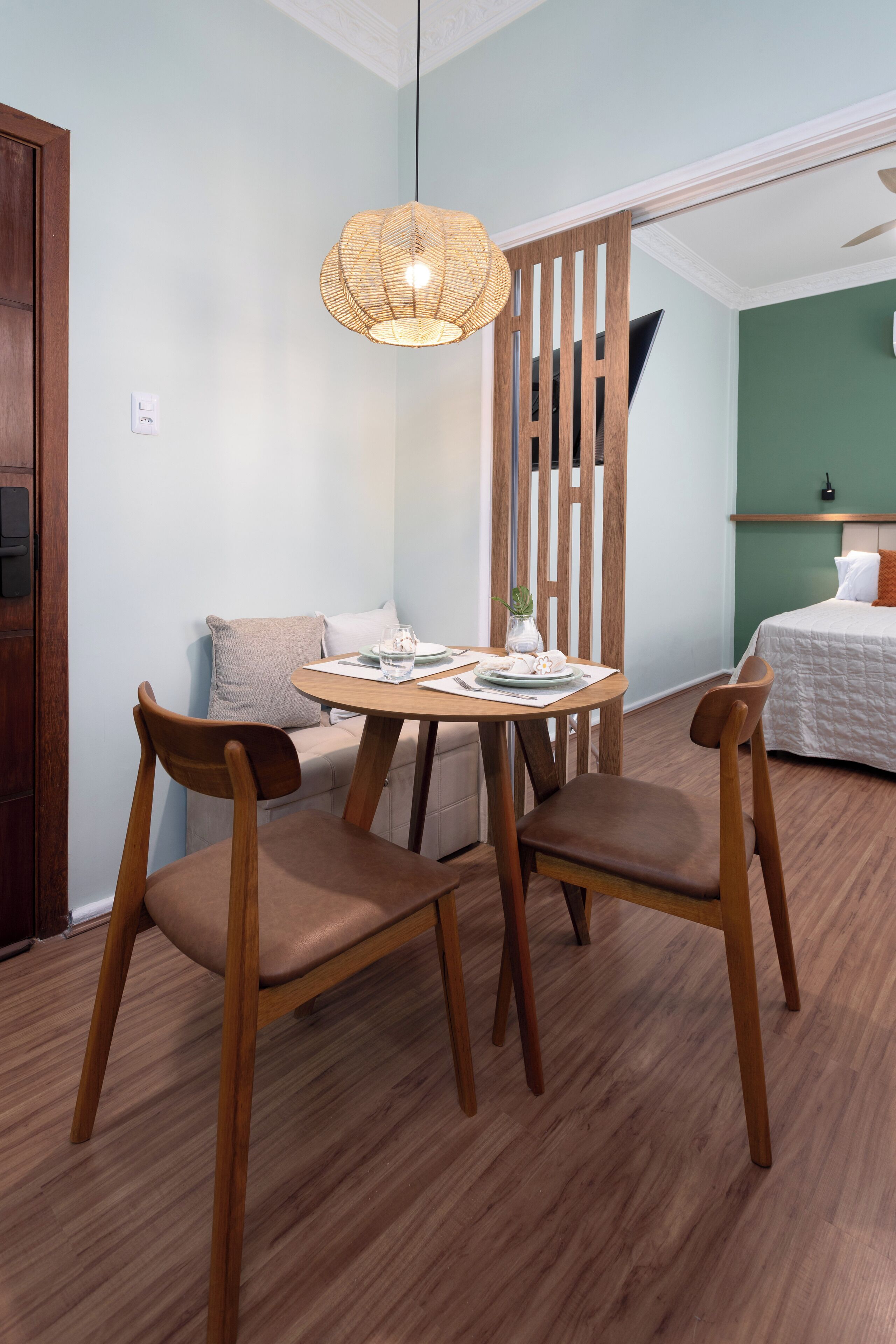 A room with a round wooden table, two chairs, a small white vase, and a hanging light fixture.