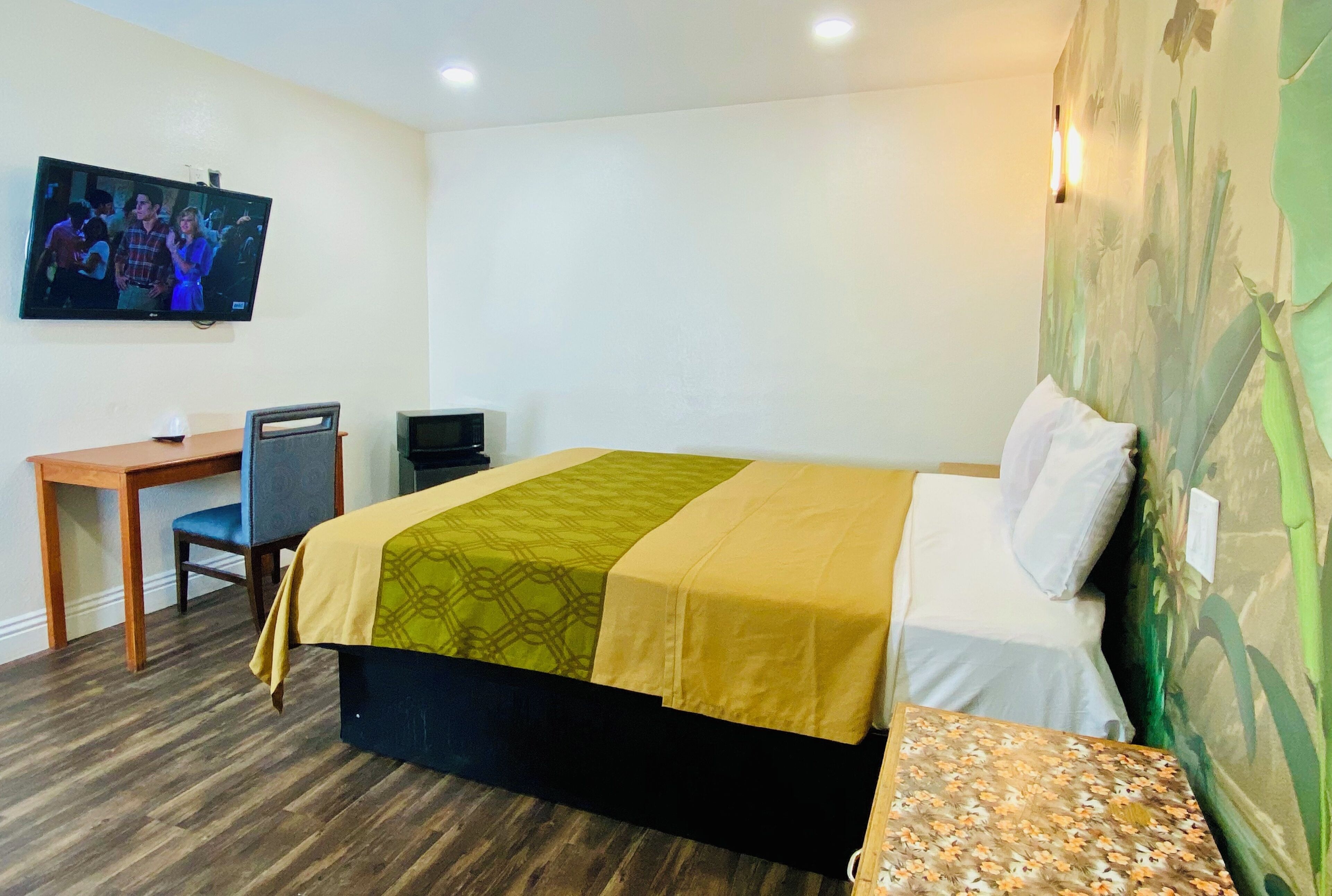 A hotel room with a bed, a desk, a chair, a television, and a wall with a floral pattern.