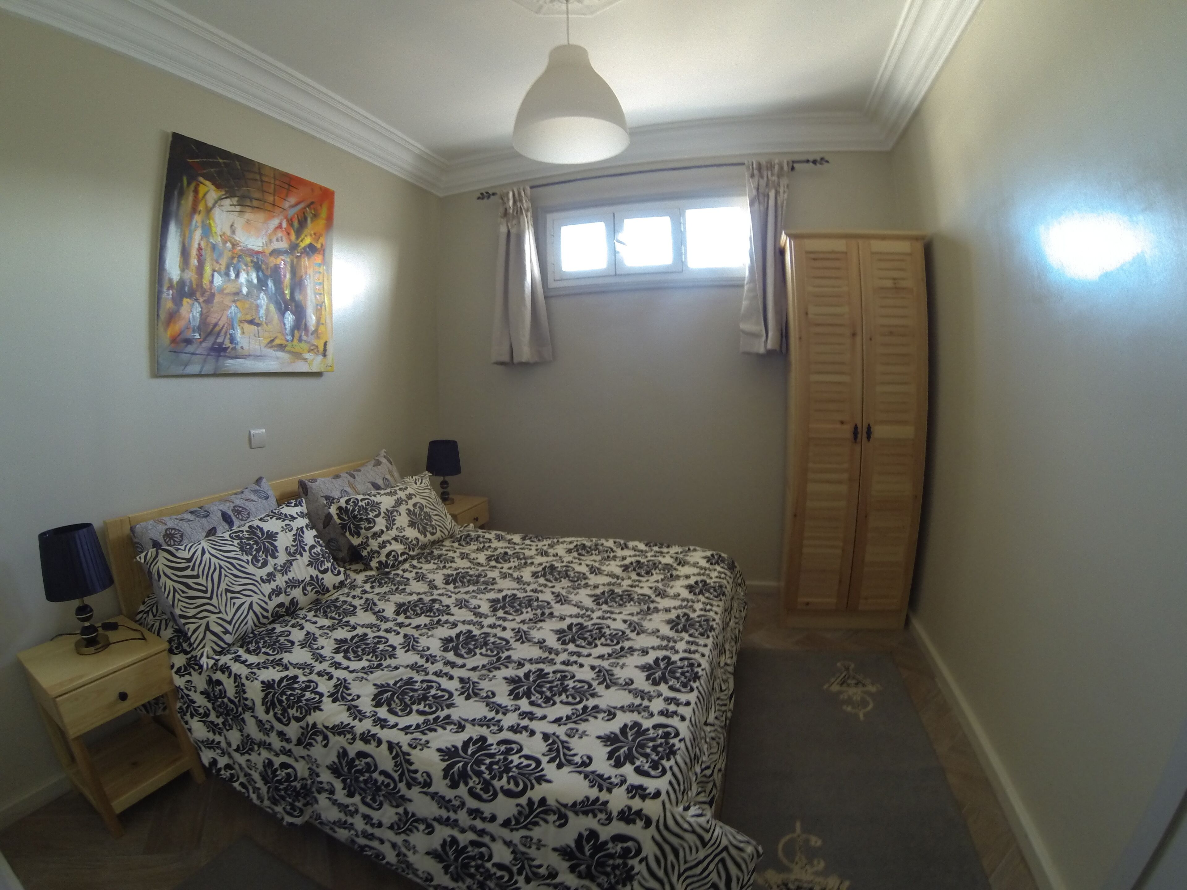 Une chambre à coucher comprenant un lit, des tables de chevet, une lampe, une armoire, un tableau et une fenêtre avec des rideaux.