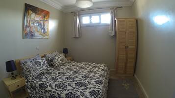 Une chambre à coucher comprenant un lit, des tables de chevet, une lampe, une armoire, un tableau et une fenêtre avec des rideaux.