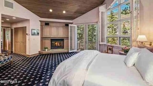 A spacious bedroom with a large bed, a fireplace, and a view of the outdoors through a large window. - Luxury Vail Mountain Estate – Ski Access • Spacious • Elegant Mountain Retreat (Vail)