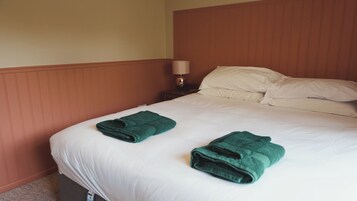 Habitación de hotel con una cama, dos toallas verdes, una mesita de noche con una lámpara y un cabecero de madera.