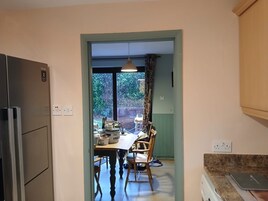 A kitchen with a dining table, chairs, a refrigerator, and a window with curtains.