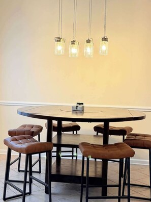 A round dining table with six stools, a chandelier with four lights, and a small object on the table. - Cozy 2-Bedroom Duplex in Little River (Little River)