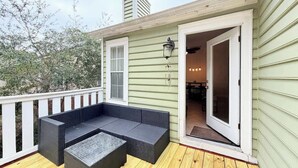 A covered outdoor seating area with a sofa and a table, a door leading to an interior space, and a white railing. - Cozy 2-Bedroom Duplex in Little River (Little River)