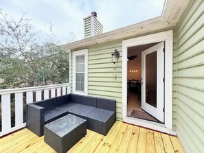A covered outdoor seating area with a sofa and a table, a door leading to an interior space, and a white railing. - Cozy 2-Bedroom Duplex in Little River (Little River)