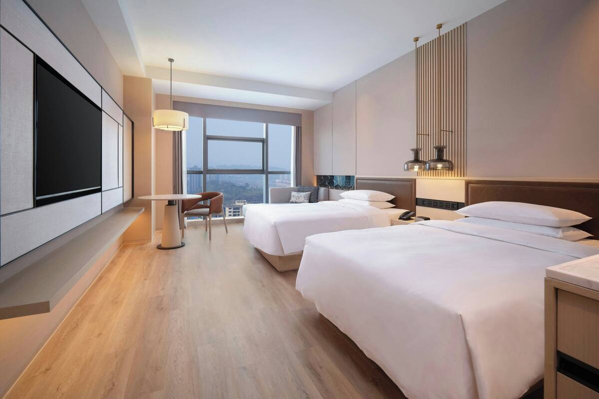 A hotel room with two beds, a desk, a chair, and a large TV.
