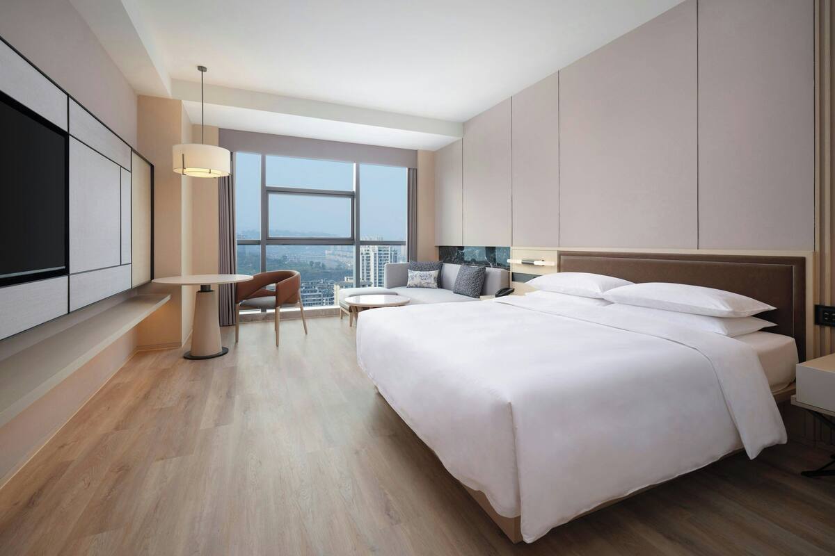 A modern hotel room with a large bed, a desk, and a view of the city.