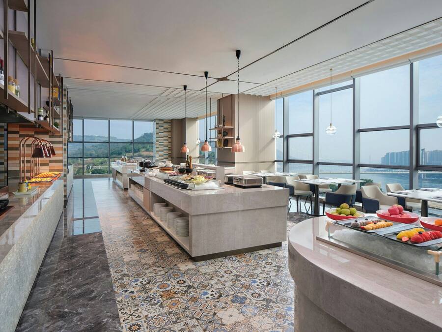 A modern hotel lobby with a central bar area, seating arrangements, and large windows offering a view of the cityscape.