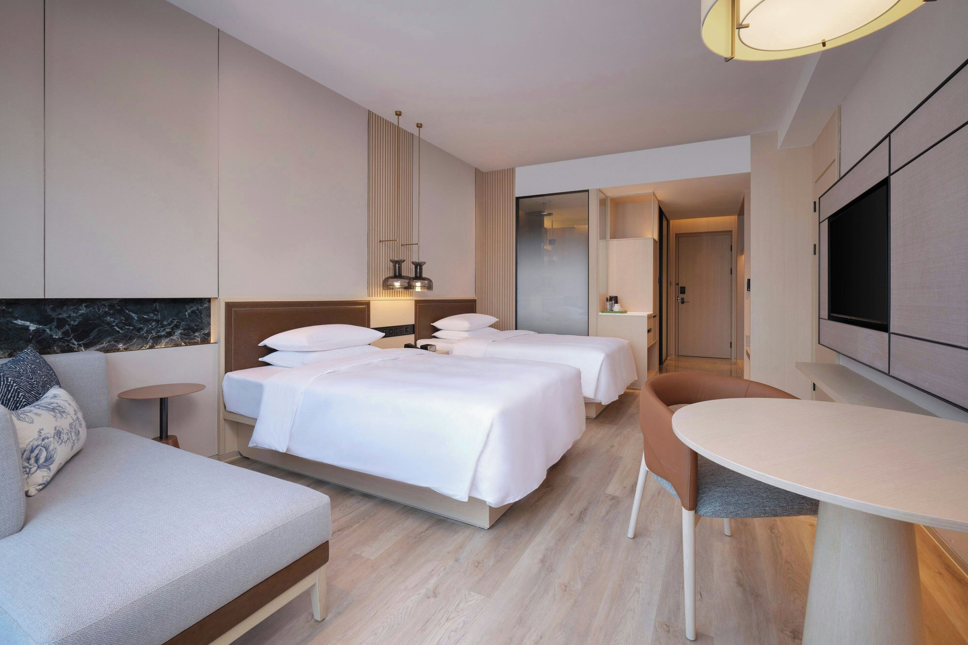Habitació d'hotel moderna amb dos llits, un sofà, una taula de menjador i una televisió.