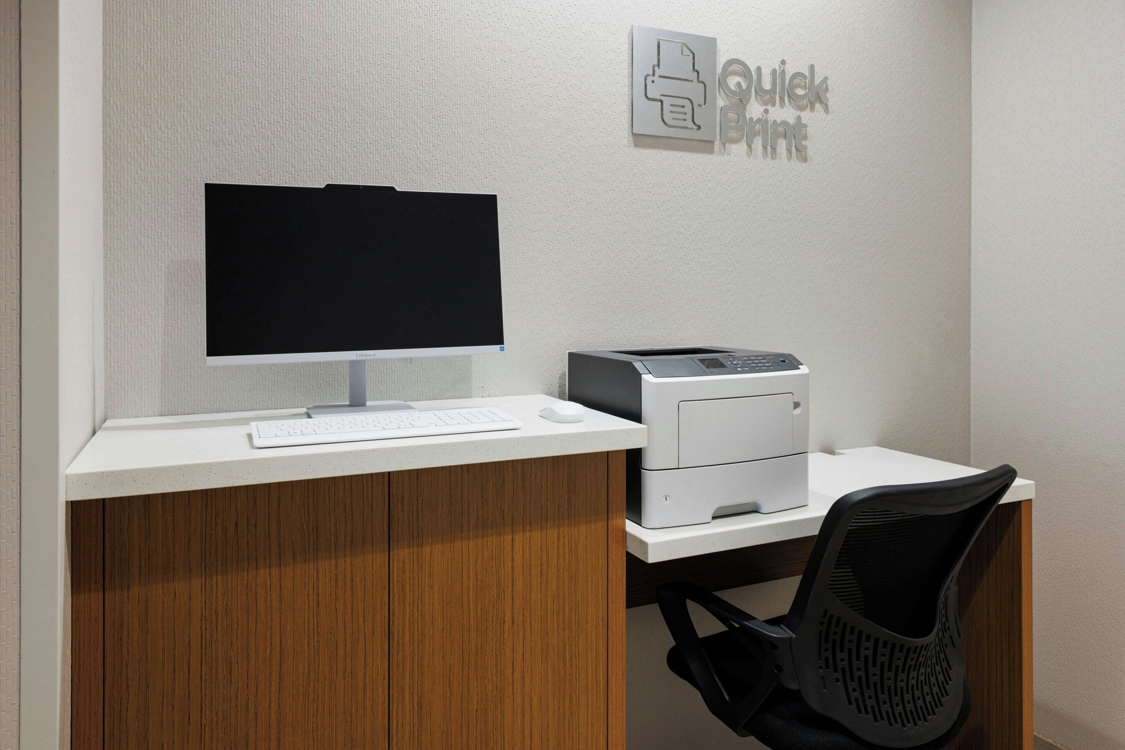 Un bureau avec un ordinateur, un clavier et une imprimante, une chaise et un panneau fixé au mur.