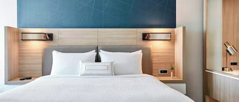 Una habitación de hotel con una cama grande, dos mesitas de noche, un armario de madera y una lámpara de pared.