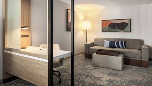 A hotel room with a bed, a desk, a chair, a sofa, a lamp, and a painting on the wall. - Springhill Suites By Marriott Madison Fitchburg (Madison)