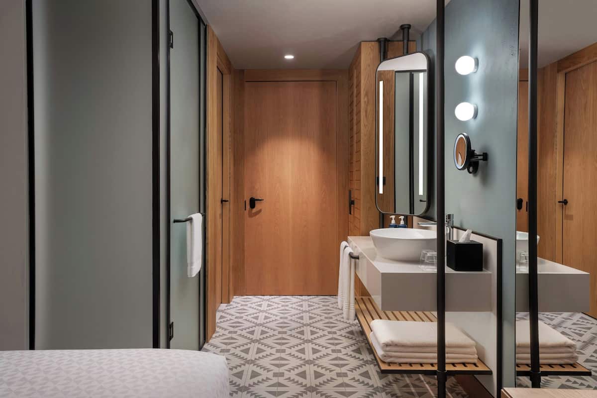 Une salle de bain moderne avec une porte en bois, un lavabo blanc, un miroir avec éclairage intégré et des carreaux de sol à motifs.
