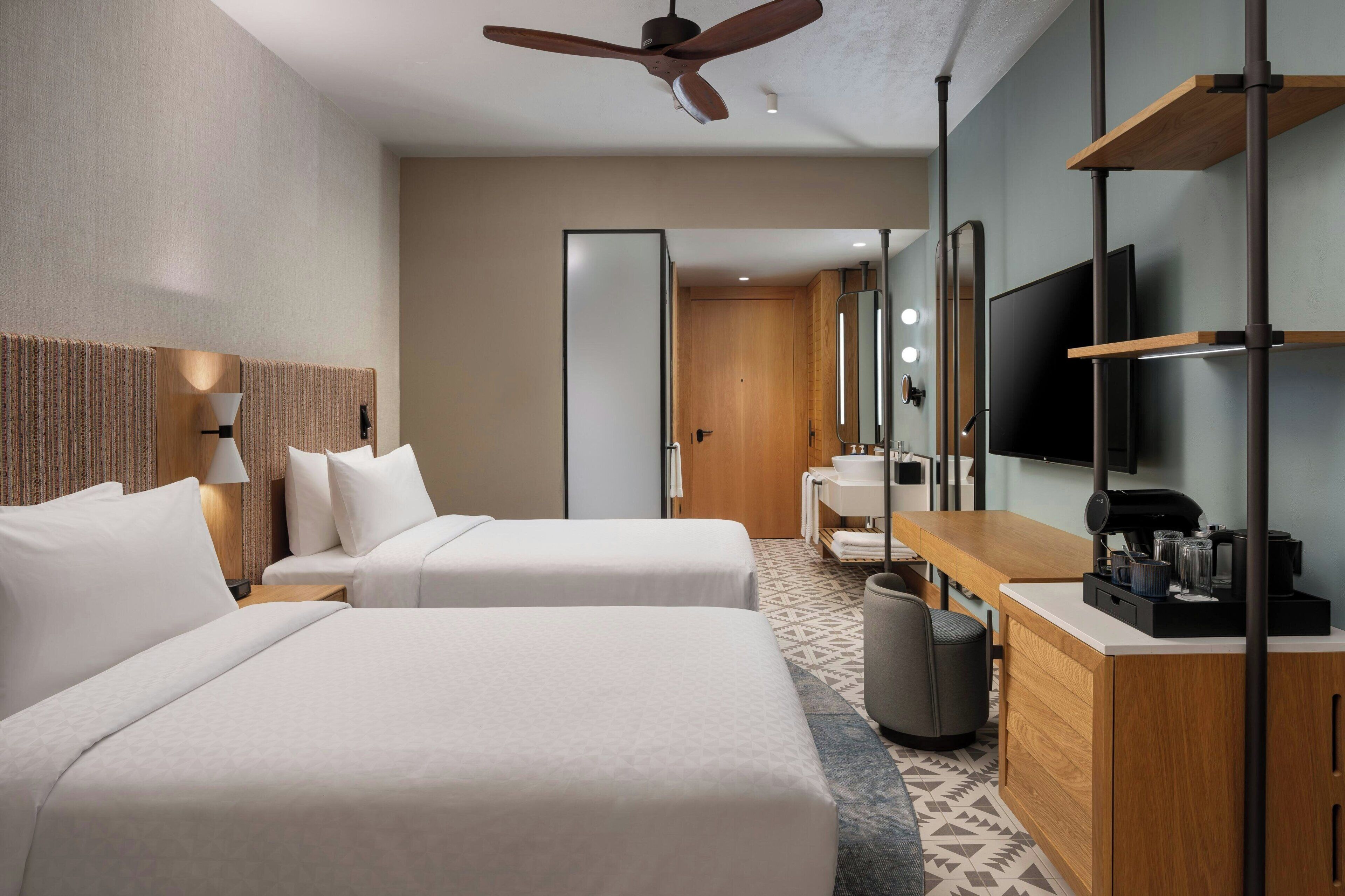 Une chambre d’hôtel avec deux lits, un bureau avec une machine à café, une télévision et un miroir.