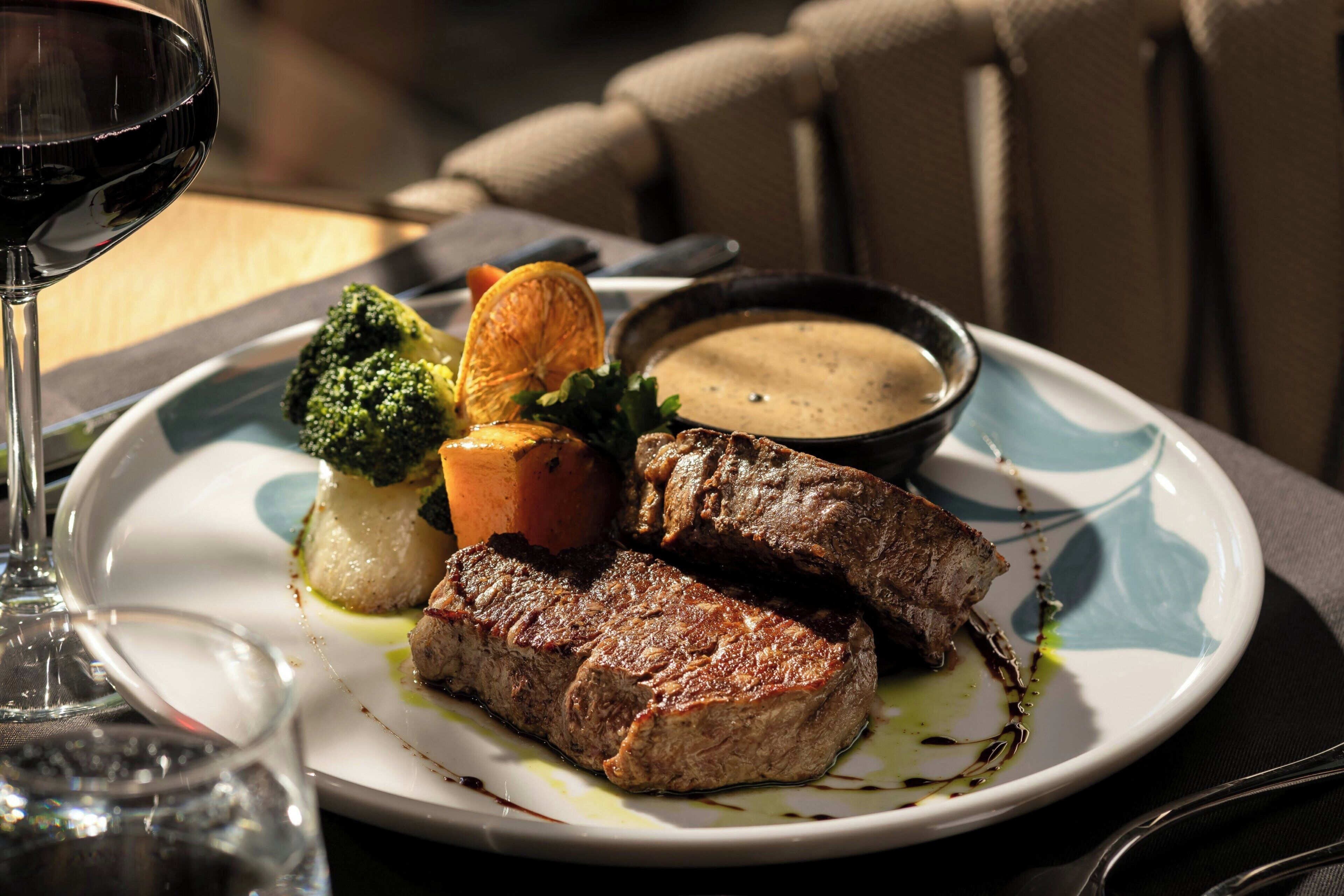 A plate with steak, broccoli, and a side of sauce.