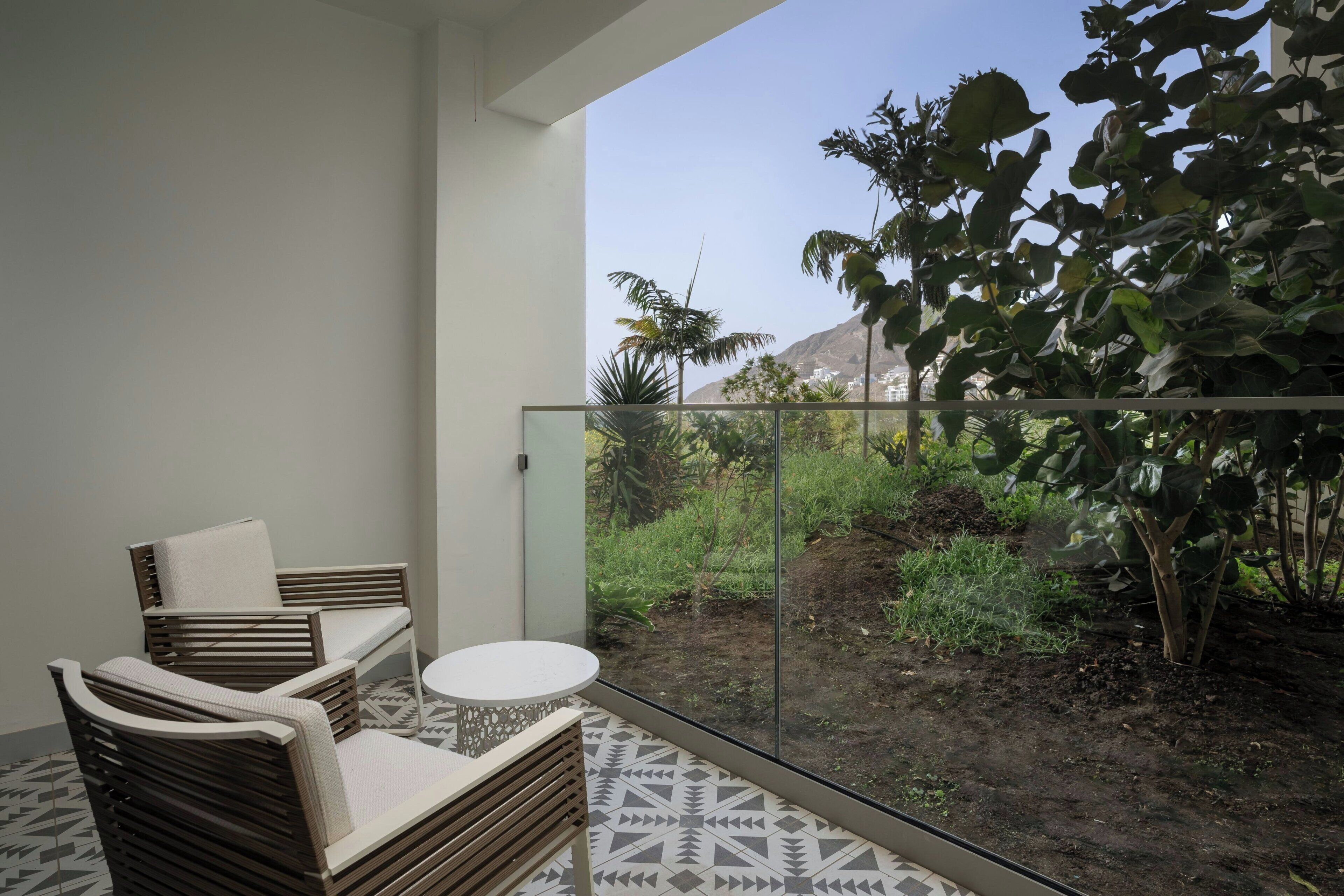 A balcony with a sofa, a small table, and a view of greenery and a mountain.