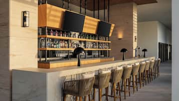 Una zona de bar con una barra larga, varias estanterías llenas de botellas y distintos taburetes.