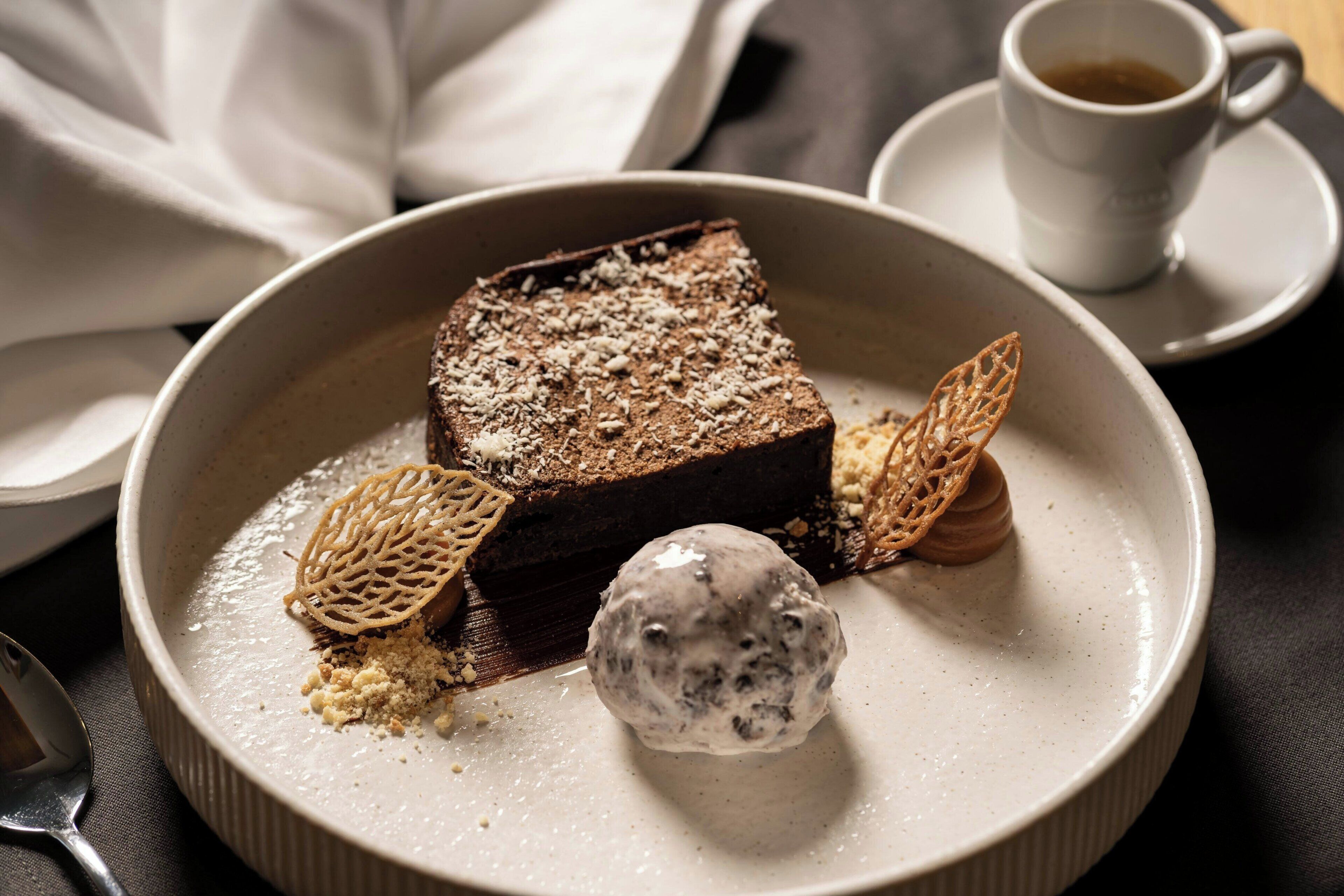 Un plato de postre con un brownie, una bola de helado y una hoja decorativa.