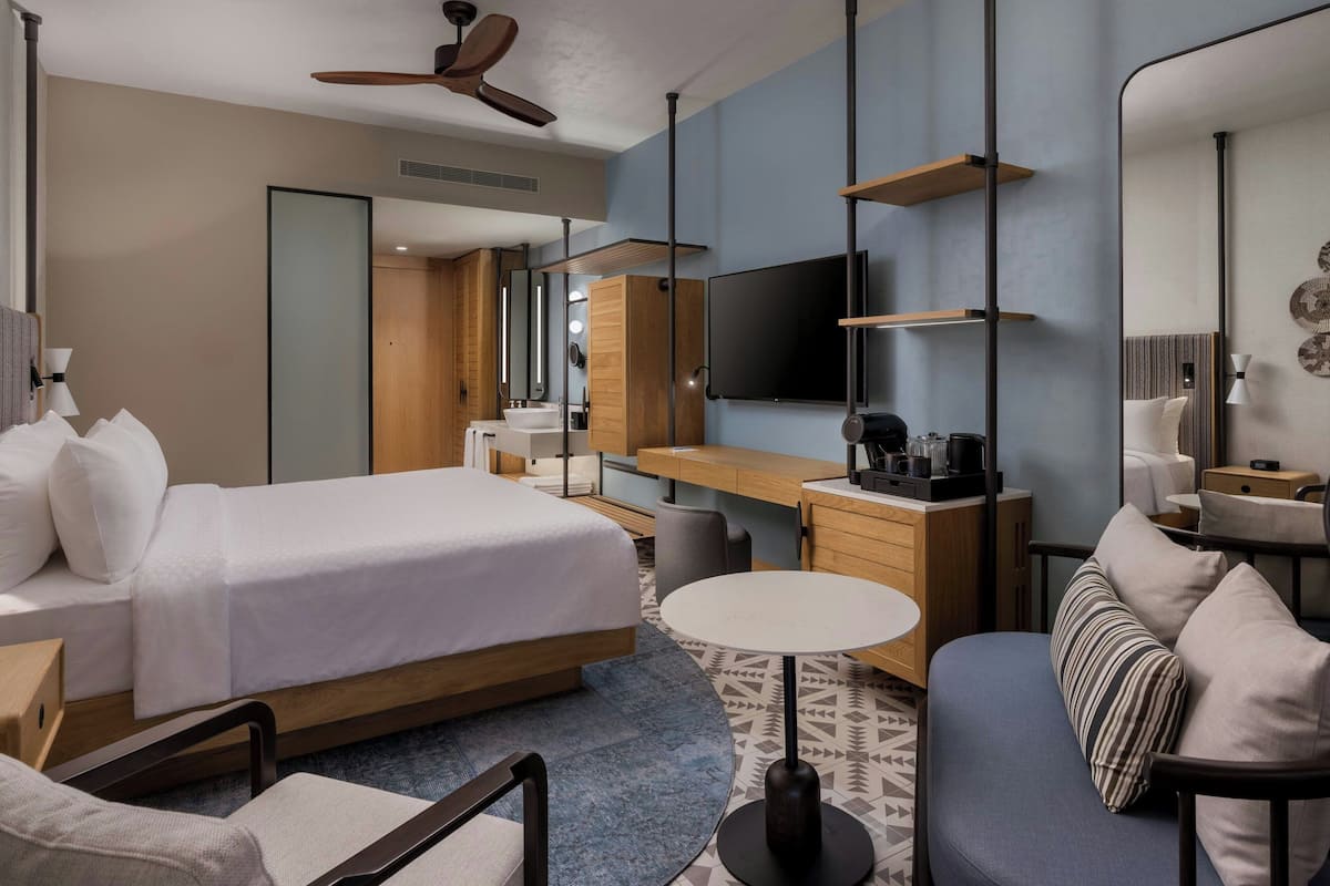 Une chambre d’hôtel moderne équipée d’un lit, d’un bureau, d’un canapé, d’une table ronde et d’un téléviseur.