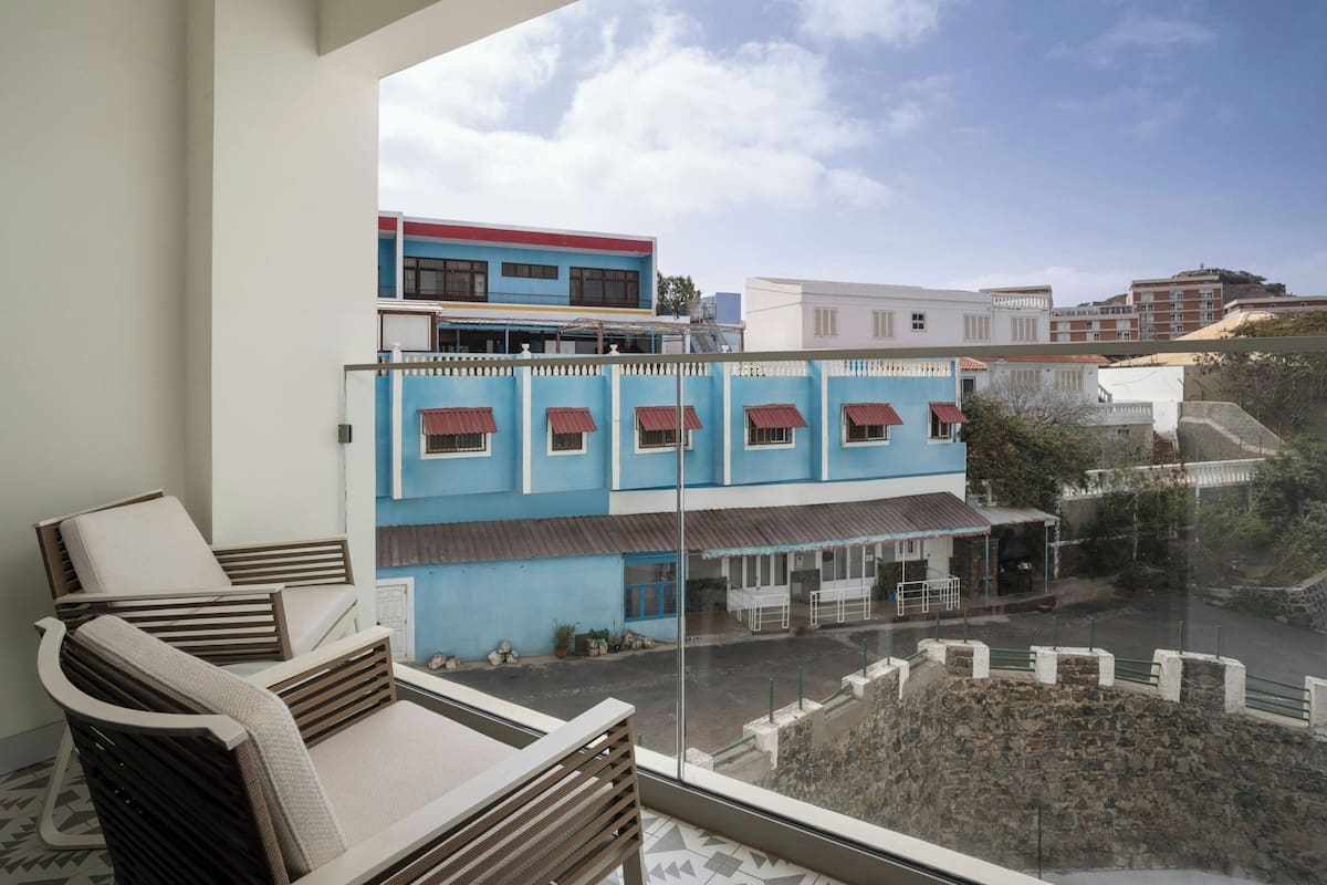 Un balcon avec vue sur un immeuble bleu, un mur de pierre et un immeuble blanc en arrière-plan.