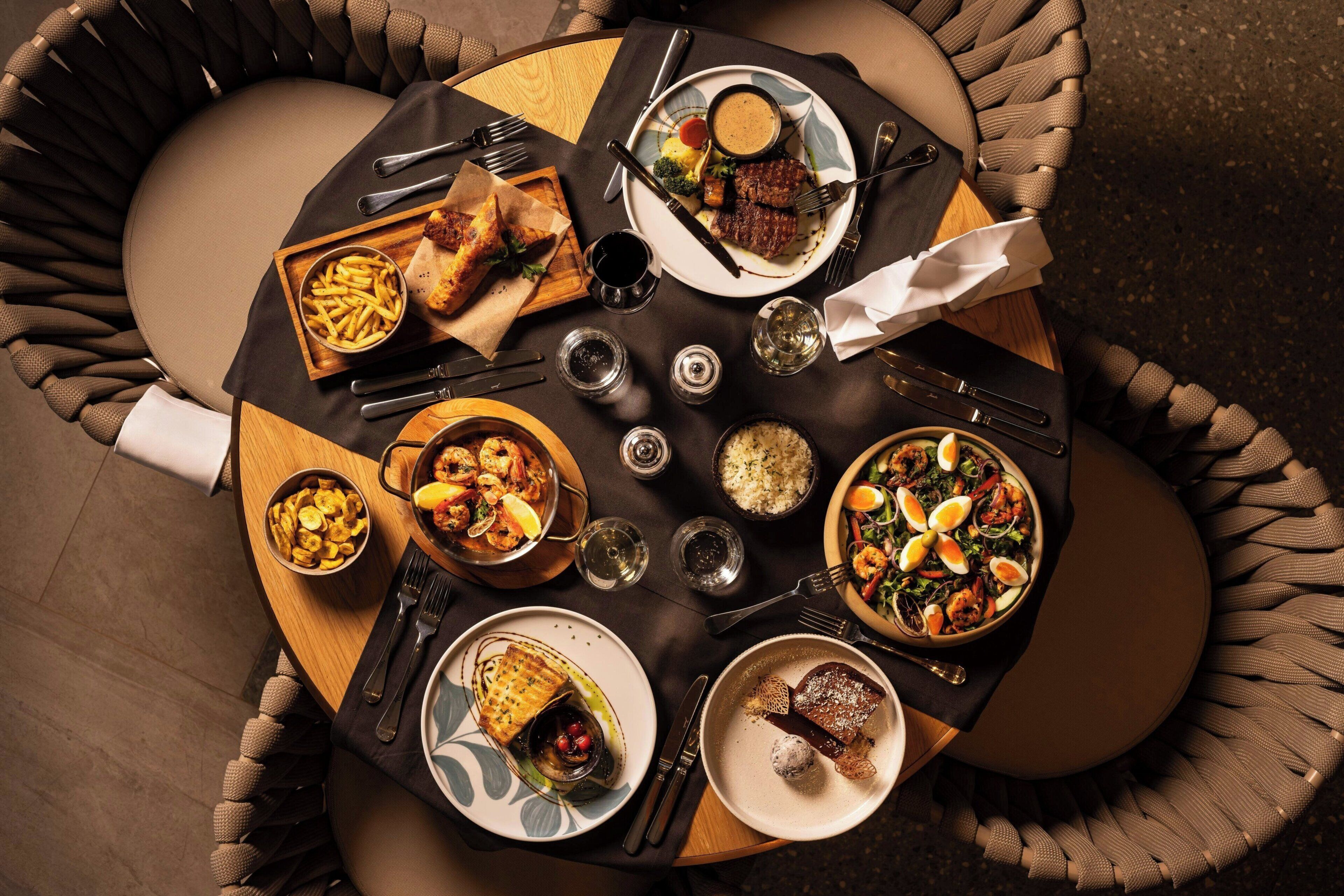 A round dining table with various dishes, cutlery, and glasses.