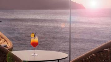 A table with a drink and wicker chairs, overlooking a body of water with a distant landmass.