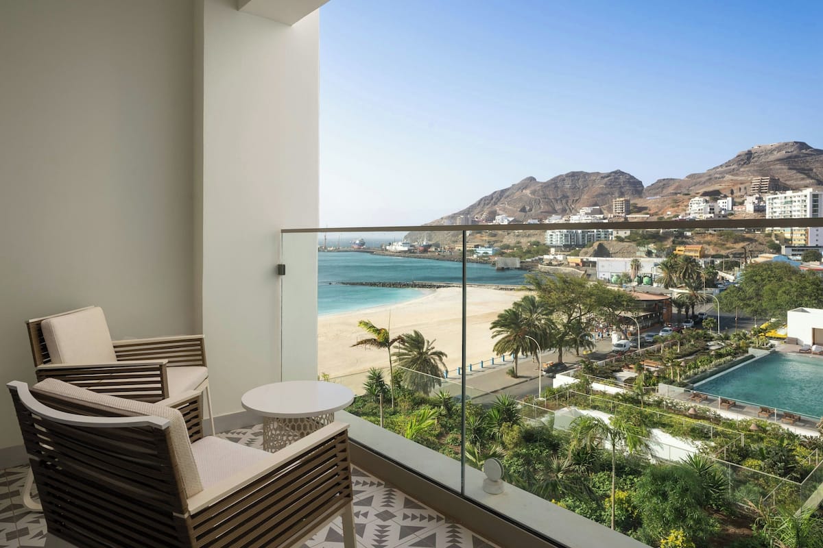 Uma varanda com vista para uma praia, uma piscina e montanhas.
