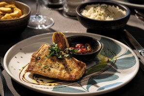 A plate with a piece of food garnished with herbs and a slice of dried fruit, accompanied by a bowl of rice and a glass of water. - Four Points By Sheraton São Vicente Resort (Mindelo)