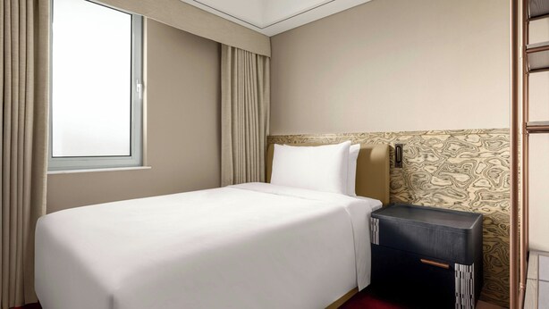 A hotel room with a single bed, a nightstand, a window with curtains, and a patterned wall. - Artik Suzhou, Apartments By Marriott Bonvoy (Suzhou)