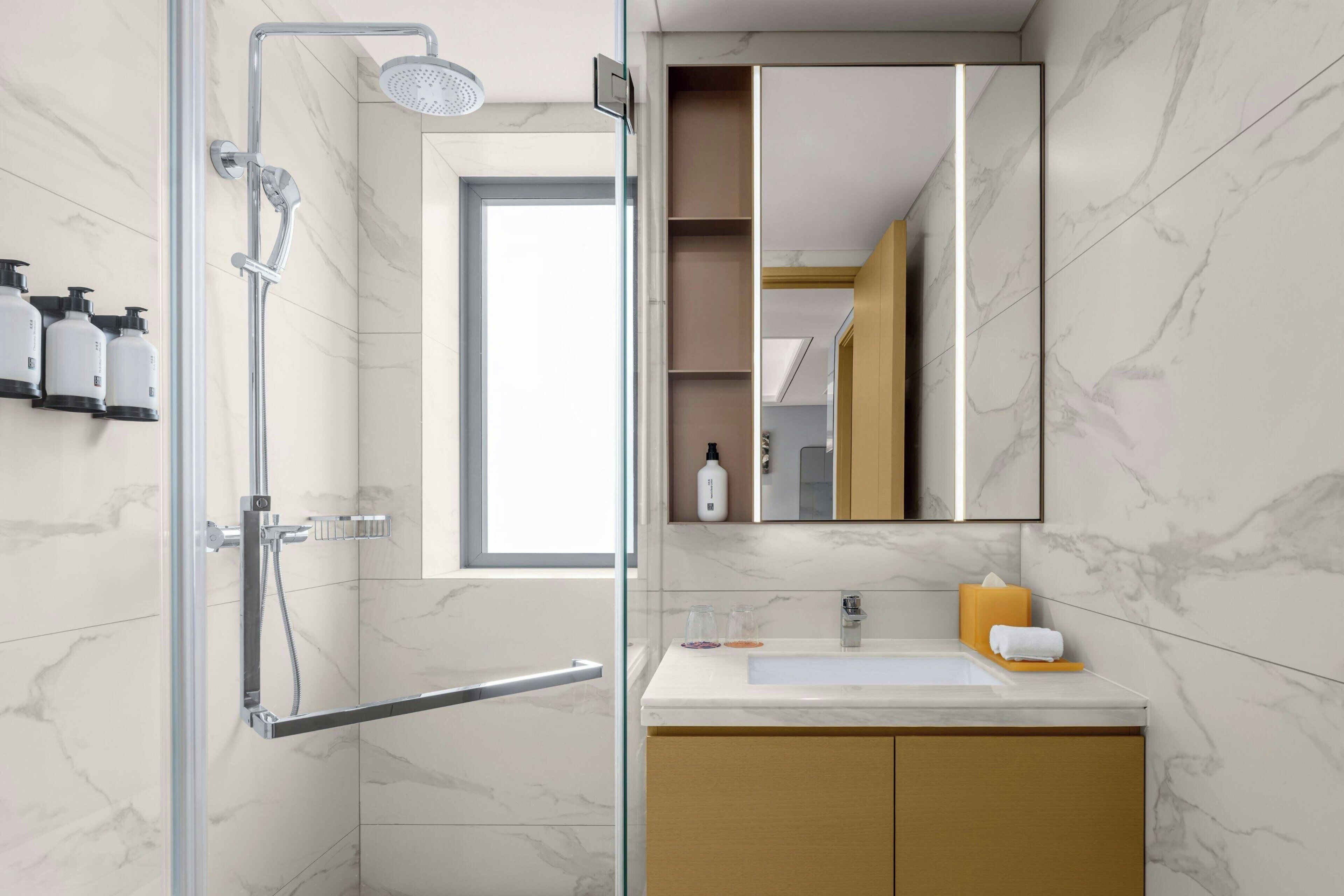 A modern bathroom with a glass-enclosed shower, a white sink, and a marble backsplash.