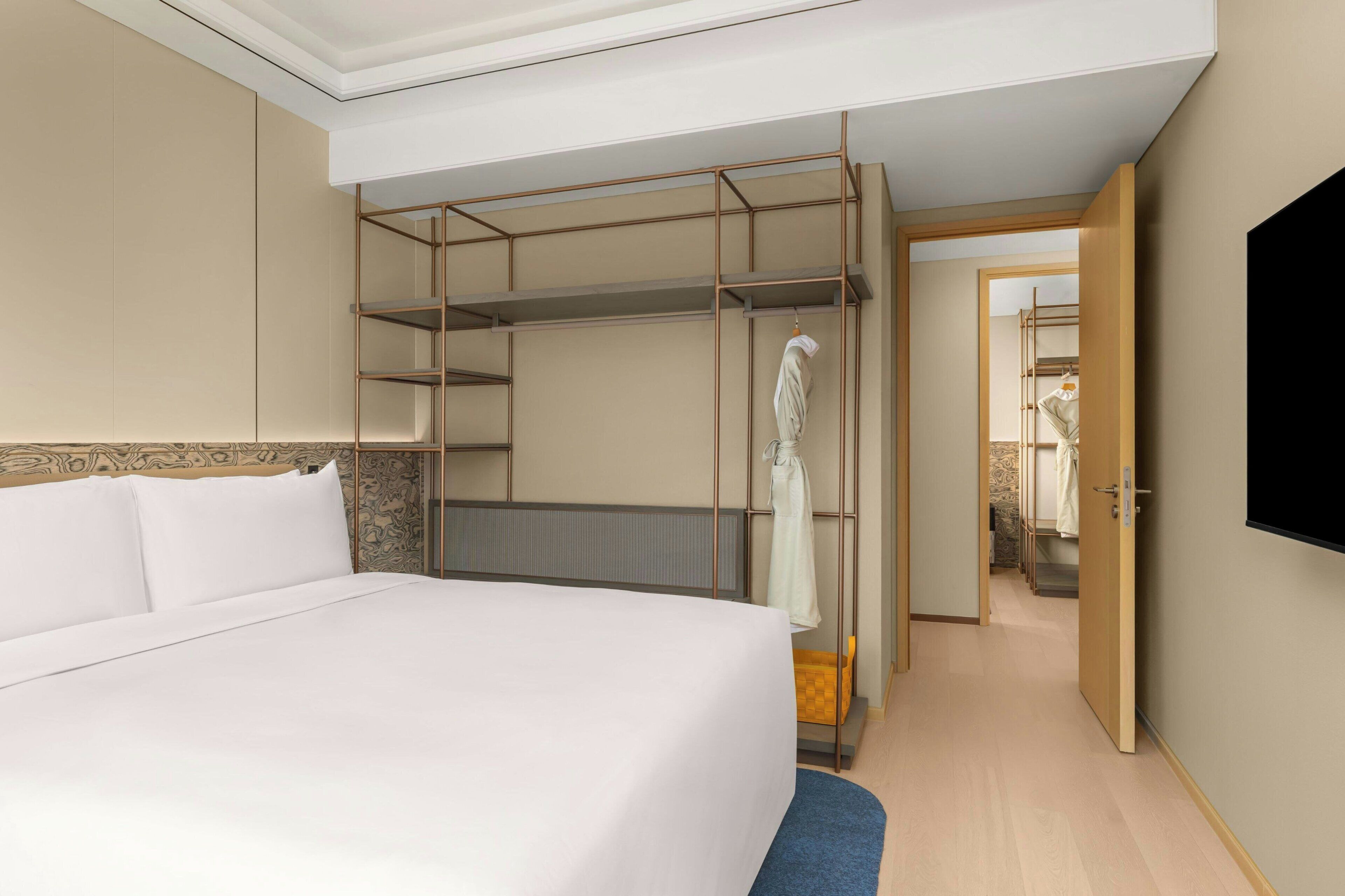 Ein Hotelzimmer mit einem großen Bett, einem Schrank mit Spiegel, einer Duschkabine und einem an der Wand befestigten Fernseher.