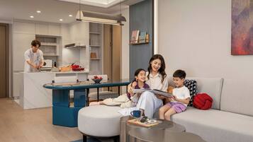 A modern living room with a sofa, a coffee table, and a dining area with a kitchen in the background.