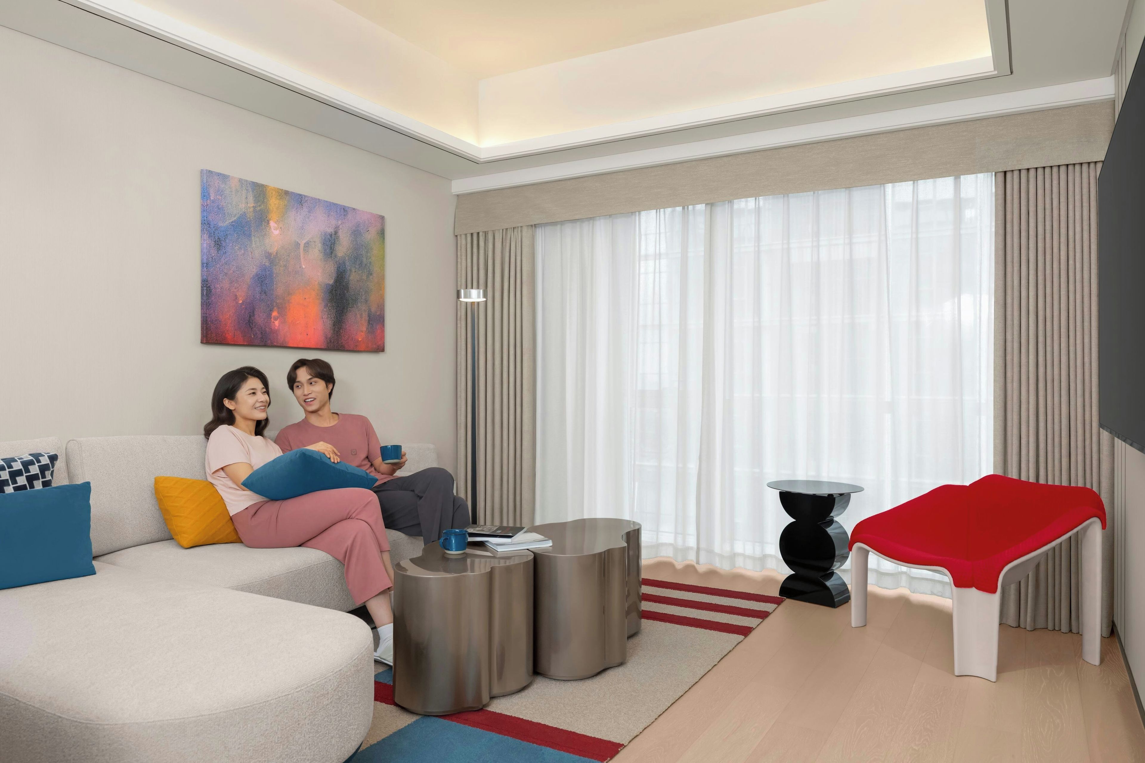 A modern living room with a sofa, a coffee table, a red bench, and a large window with curtains.