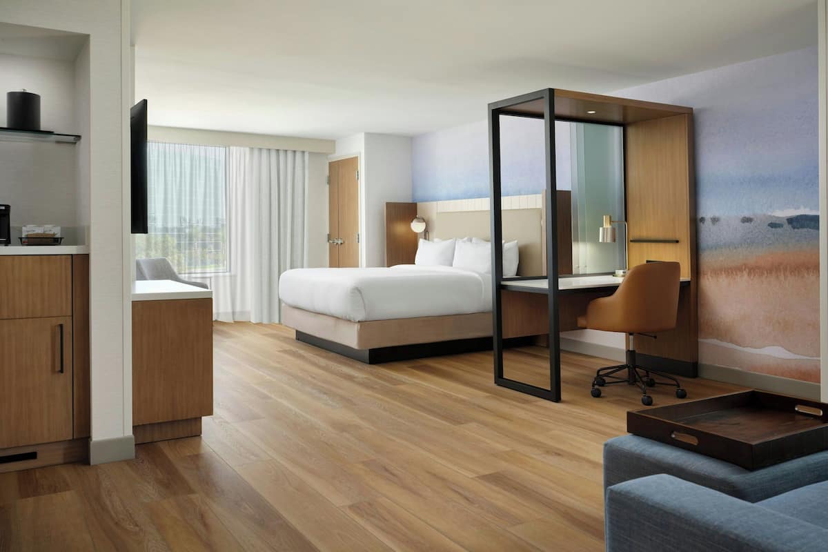 A hotel room with a bed, a desk, a chair, a TV, and a large window.