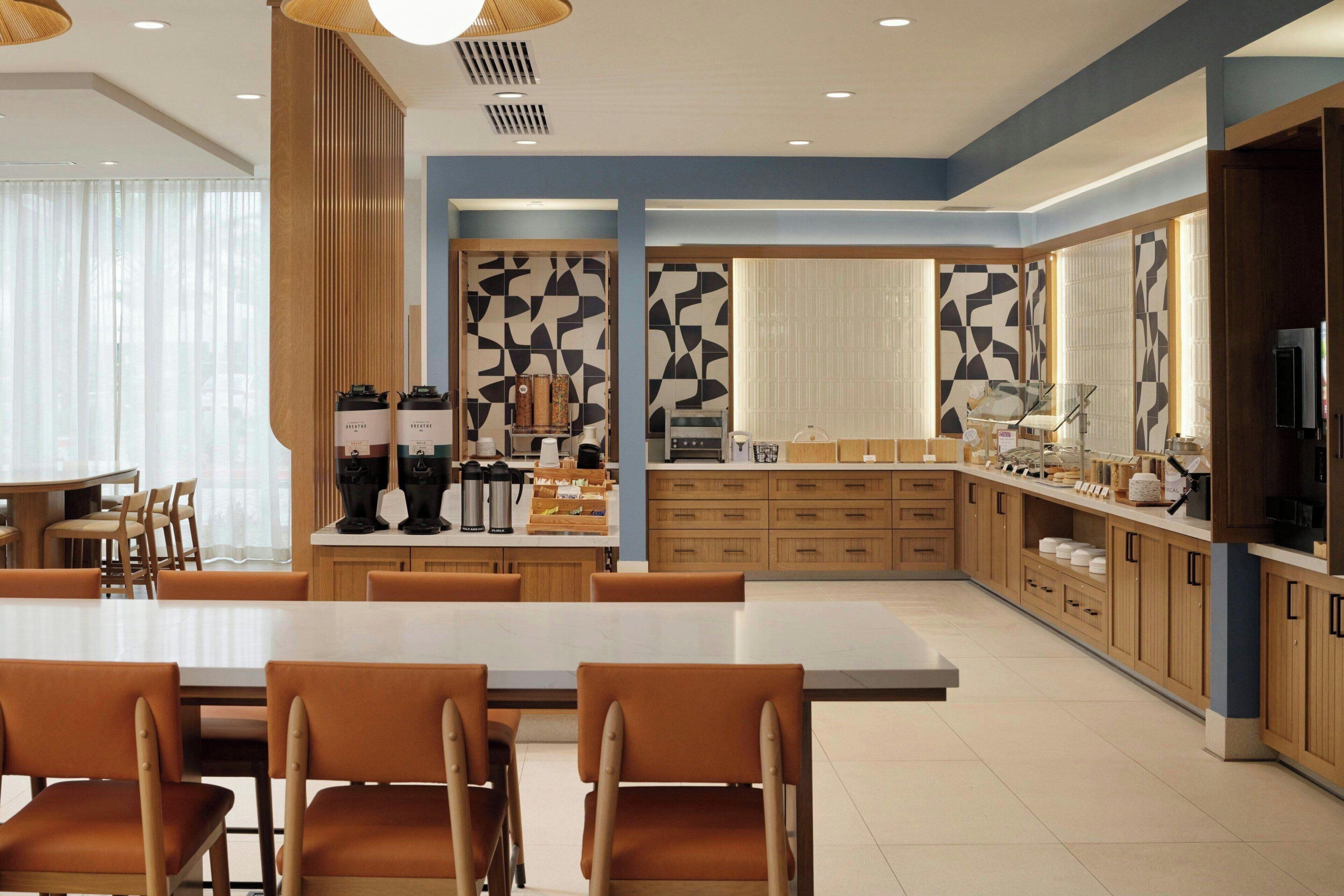 Une cuisine moderne dotée d’un îlot central, de meubles en bois et d’un coin repas avec des chaises orange.