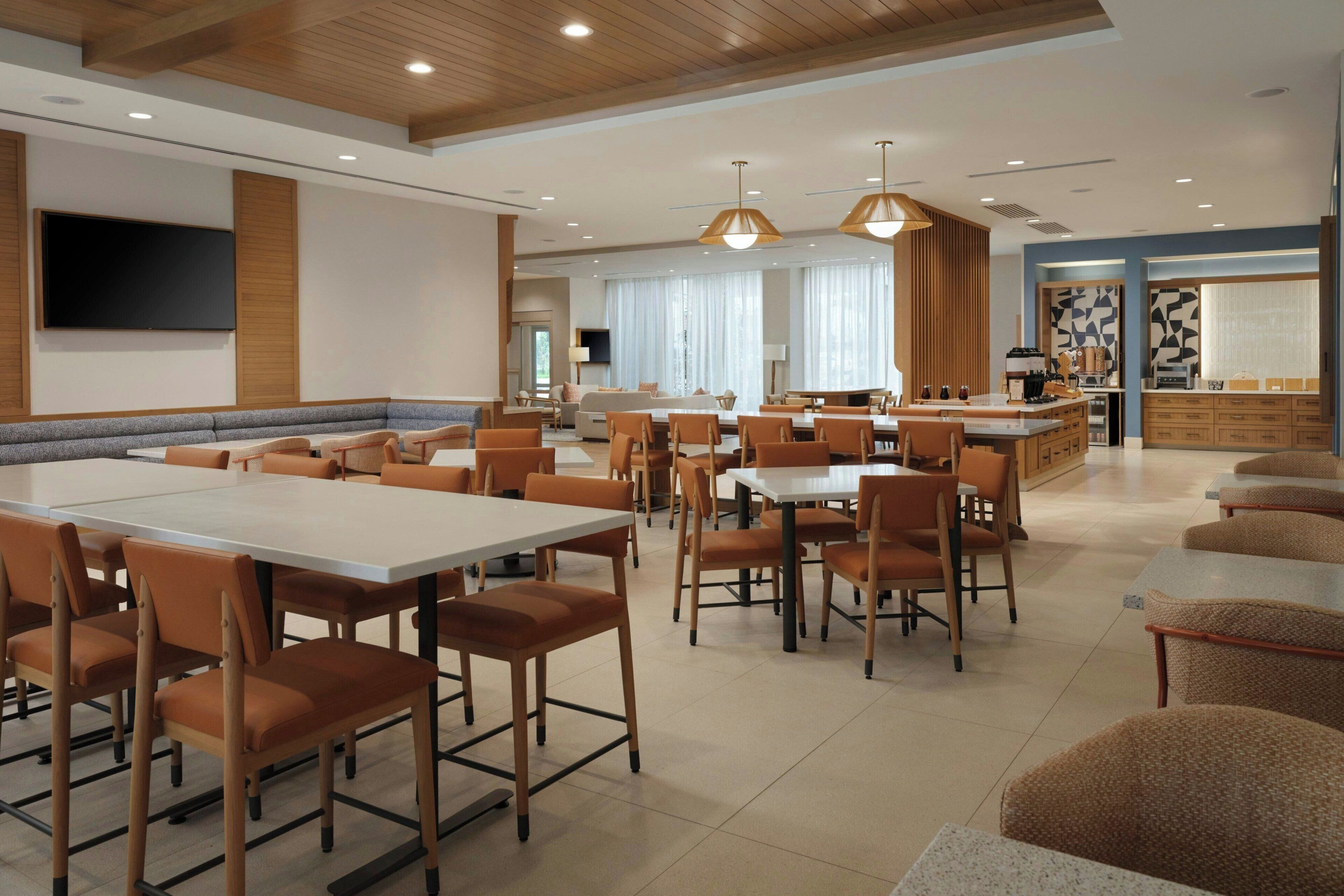 A spacious dining area with multiple tables and chairs, a kitchen area, and a seating area with sofas.