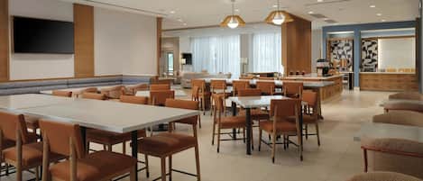 A spacious dining area with multiple tables and chairs, a kitchen area, and a seating area with sofas.