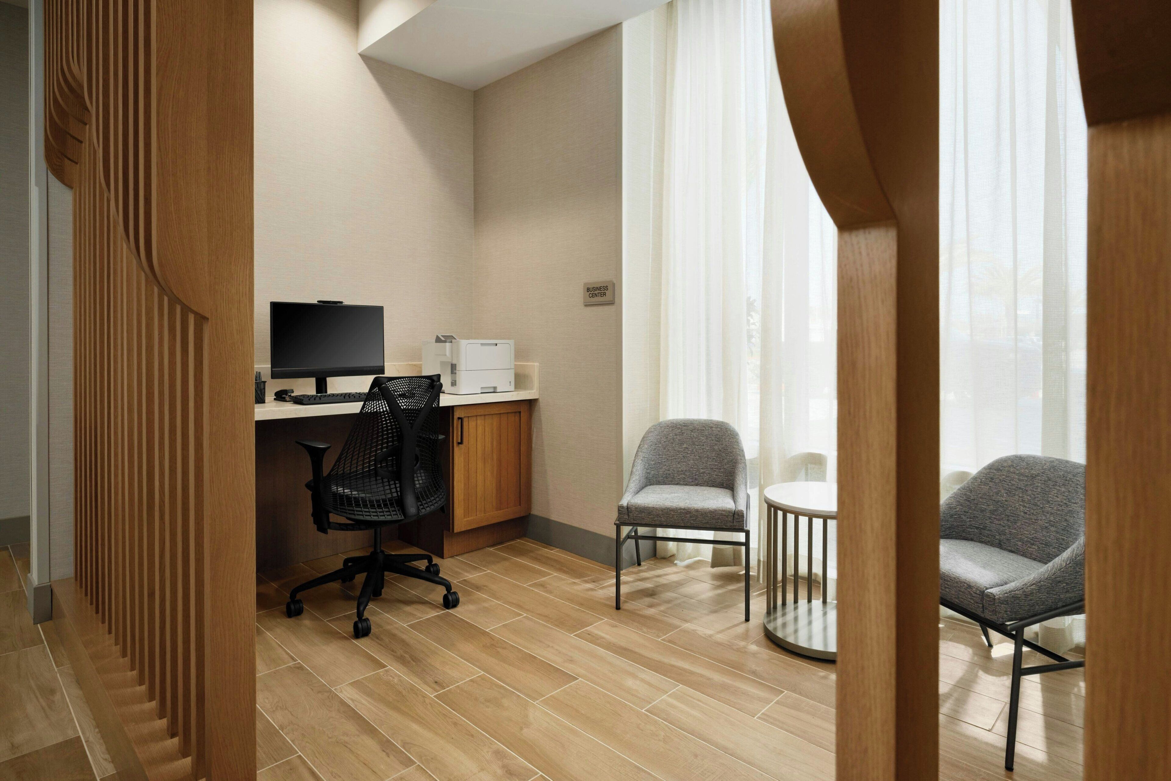 A modern office space with a desk, computer, office chair, and two armchairs.